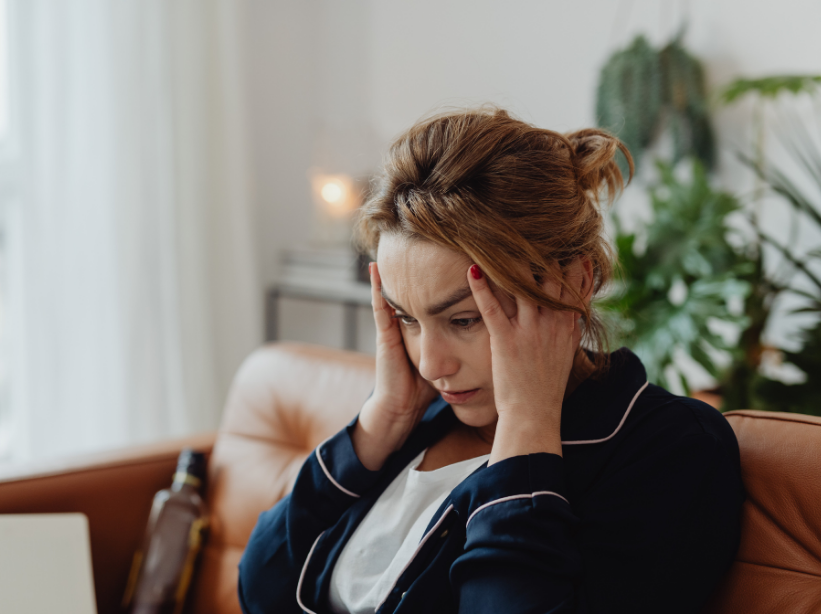 Woman with hands on head, looking down with a stressed expression; sitting on a brown couch.