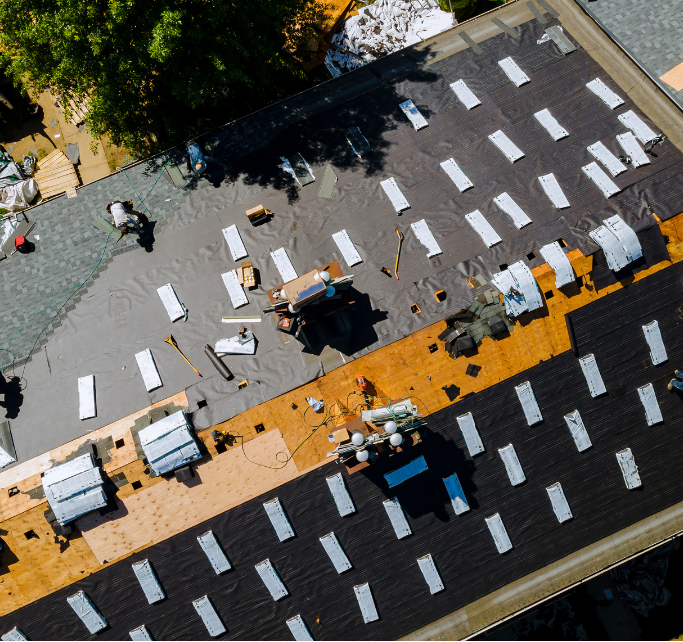 Overhead view of a roof under construction; workers, materials, and exposed layers of roofing.