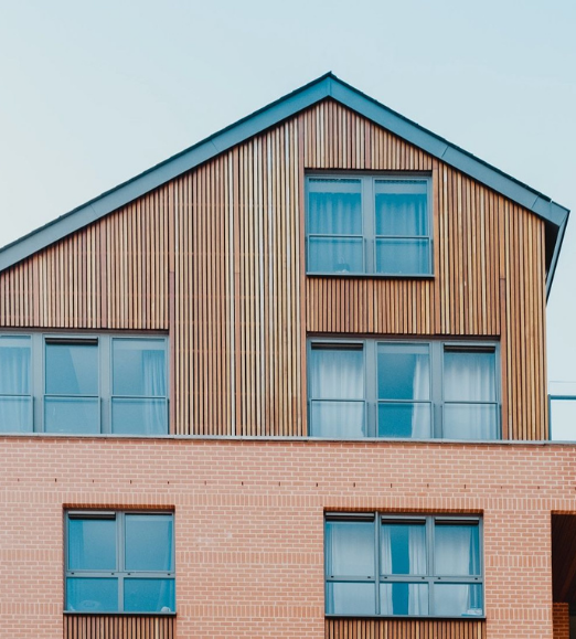 Modern building with brick base and wooden upper level, featuring multiple windows.