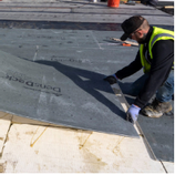 Man in safety vest installing a gray building material on a rooftop, with a close-up view.