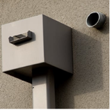 Gray metal downspout with a square top, and a pipe on a light brown wall.