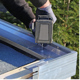 Person in gloves using a power drill to install a metal gutter on a roof.