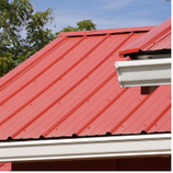 Red metal roof with white gutters against a blue sky.