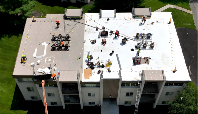 Workers on a building roof, replacing a section of the roofing. The old roof is dark, new roof is bright white.