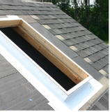 A roof with an open skylight frame; wood structure; gray shingles.