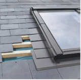 Skylight installation on a slate roof. Partially removed tiles reveal wooden beams and underlayment.