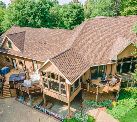 Brown roofed house with multiple decks, surrounded by trees.