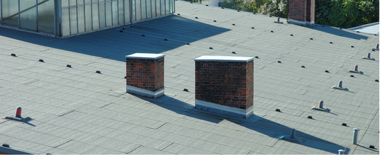 A rooftop with two brick chimneys, with a glass structure in the top left.