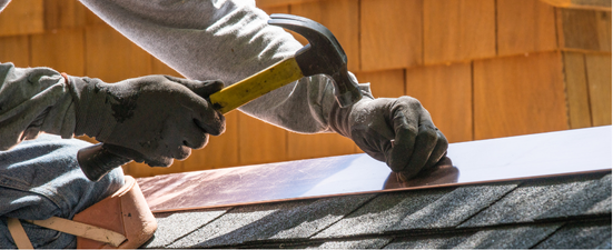 Person hammering copper flashing on a roof edge.
