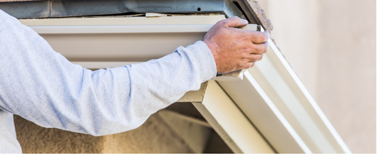 Person installing a white gutter on a building's exterior.