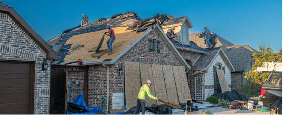 Roofers replacing a damaged roof on a house, under a clear blue sky.