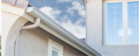 Exterior of a house with a gray gutter, a window, and a cloudy blue sky.