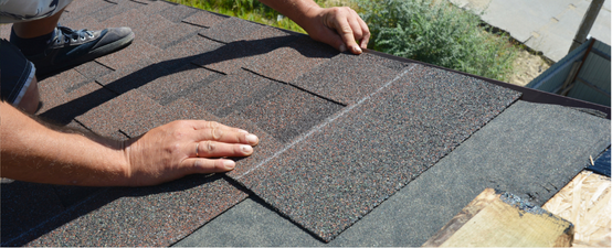 Person installing asphalt roof shingles outdoors.
