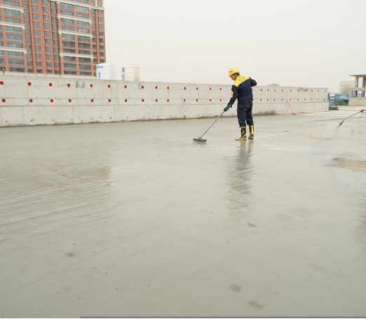 Construction worker smoothing wet concrete with a long-handled tool on a large, flat surface.