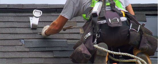 Roofer repairing asphalt shingles while wearing a safety harness and tool belt.