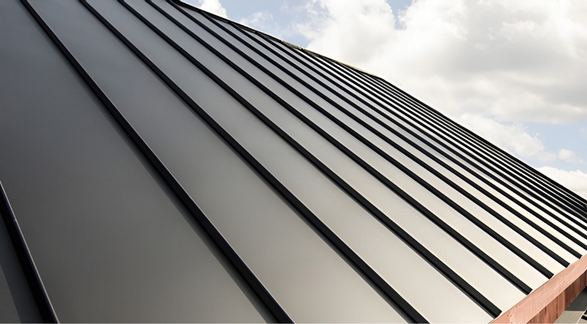 Dark gray metal roof with vertical, ridged panels against a partly cloudy sky.