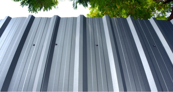 Gray shingled roof of a house with a turret and curved architectural elements. Sunny day.