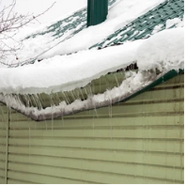 Snow and icicles on a green roof, above green siding.