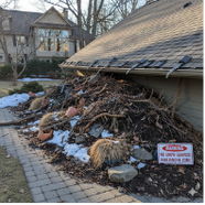 A large pile of debris next to a house with a warning sign. Partially snow-covered ground, brick walkway.