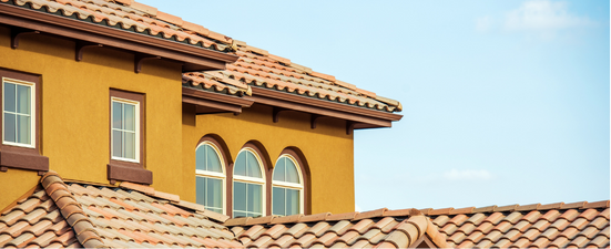 Yellow stucco house with terracotta roof tiles against a blue sky.