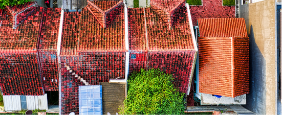 Overhead view of several buildings with orange tiled roofs, trees, and a light-colored wall.