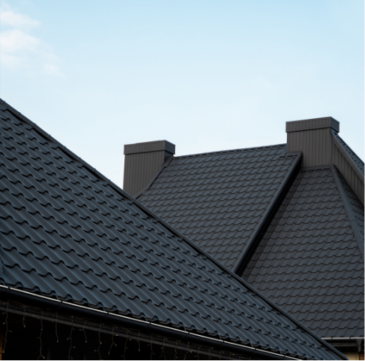 Dark gray metal roofs with chimneys against a light blue sky.