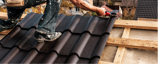 A person installs dark brown metal roofing on wooden rafters.