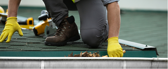 A person in yellow gloves cleans debris from a rooftop gutter.