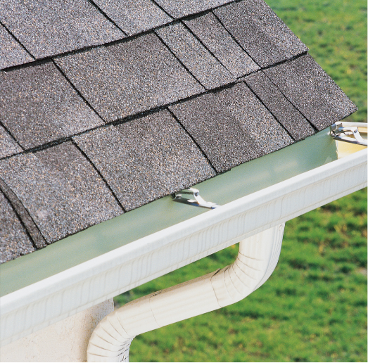 Gray shingled roof with a white gutter and downspout, set against a green lawn.