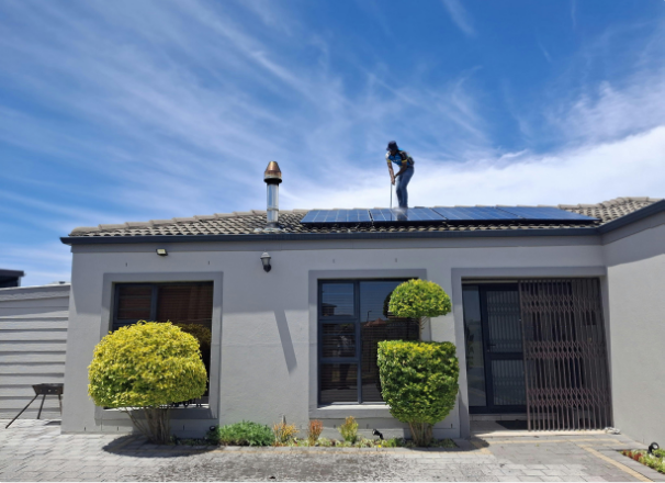 Person on roof installing solar panels on a gray house with blue sky background.