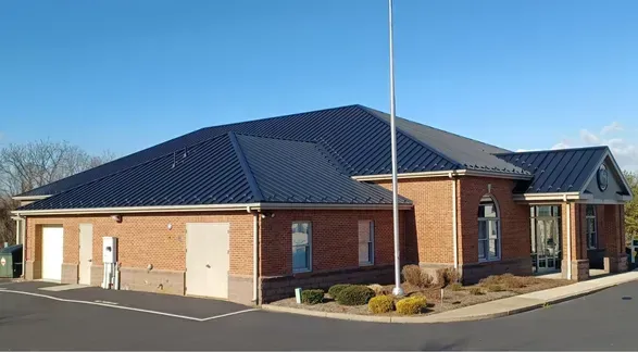 Brick building with dark blue metal roof and flag pole, under a clear blue sky.