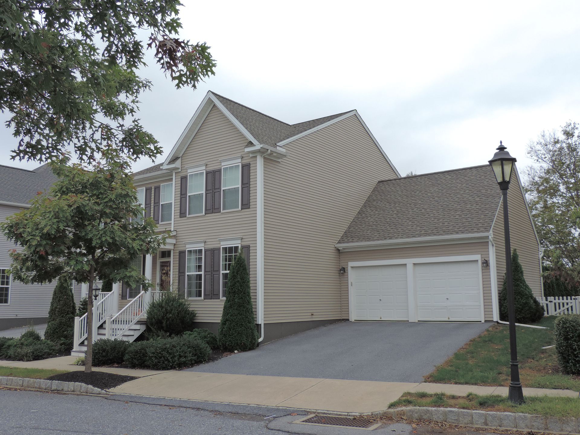 Two-story beige house with a two-car garage, brown roof, and dark gray driveway.