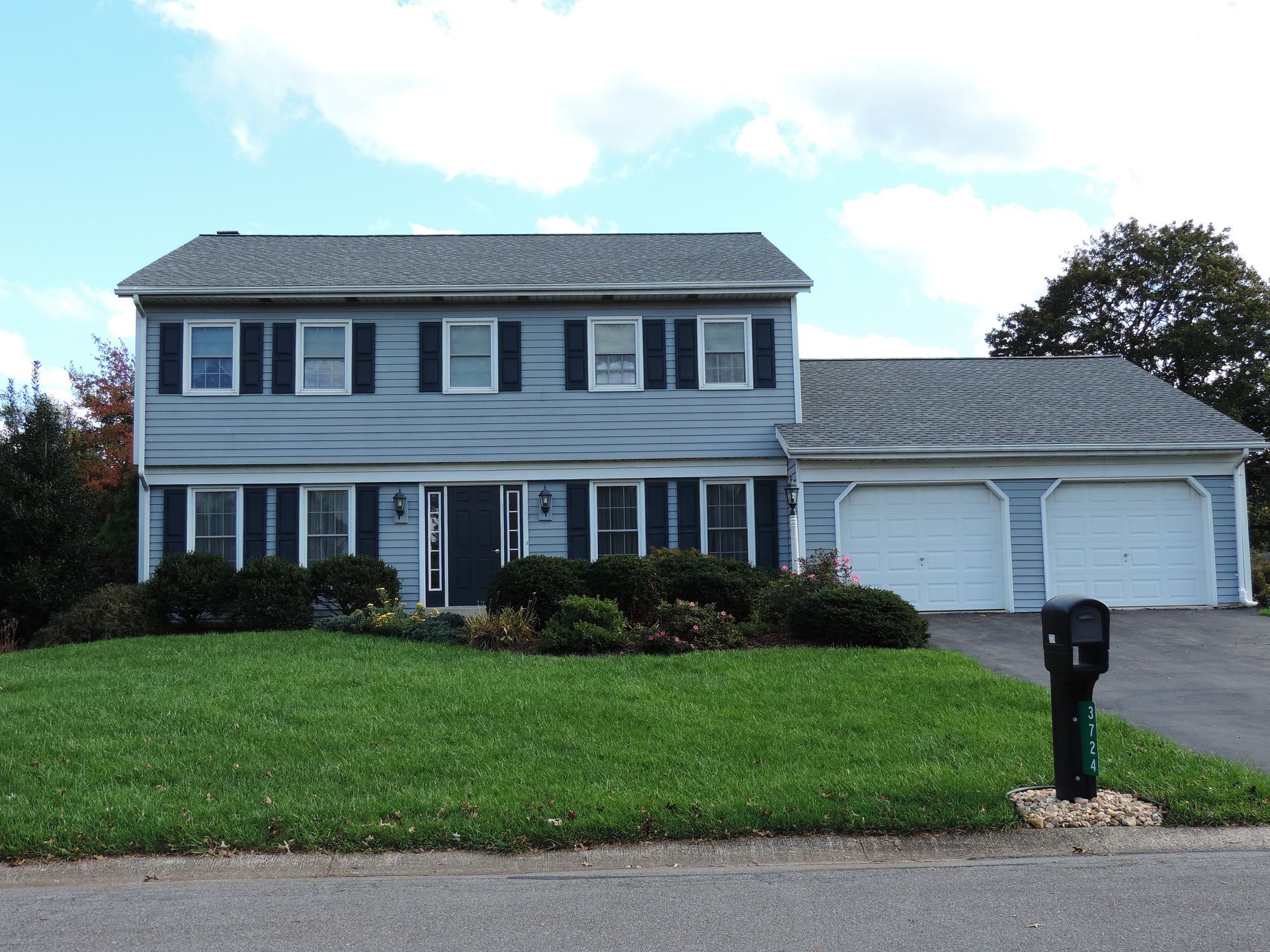 Man on a ladder installing a white gutter on a white house under a blue sky.