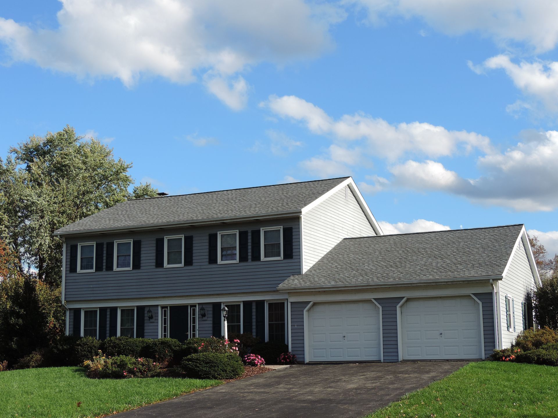Two-story gray house with black shutters, two-car garage, and blue sky with clouds.