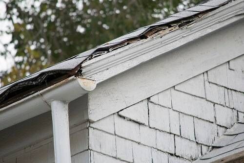 Damaged roof shingles and guttering on a white house.