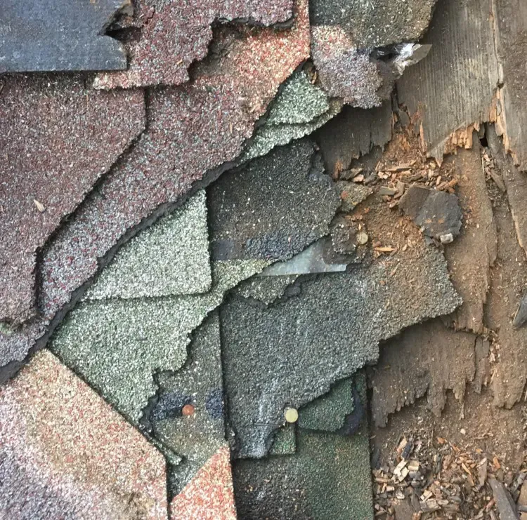 Damaged asphalt shingles on a roof, revealing the wooden underlayment.