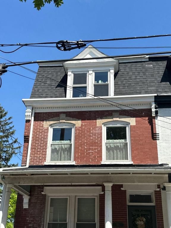 Red brick city house with a dark roof and white trim under a clear blue sky.