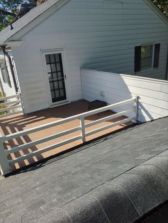 Small white house with a roof deck featuring a white railing and a brown deck floor.