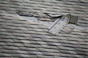 Damaged asphalt shingle roof with missing and torn shingles.