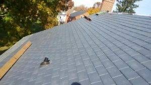 Gray asphalt shingle roof, with a chimney in the background. A wooden plank lies on the roof.