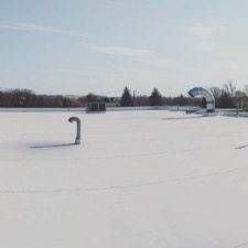Snow-covered field with a pipe and an arched structure under a clear, blue sky.