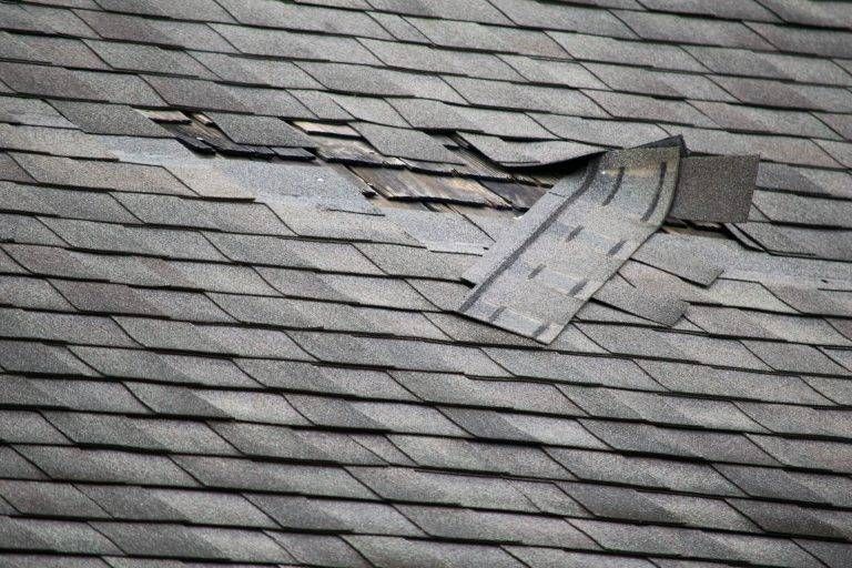 Damaged asphalt shingle roof with missing and torn shingles.