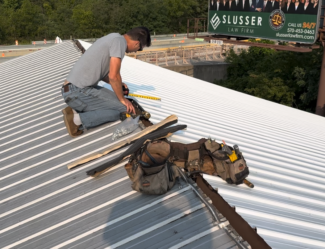 Person working on a corrugated metal roof, wearing work belt with tools, measuring.