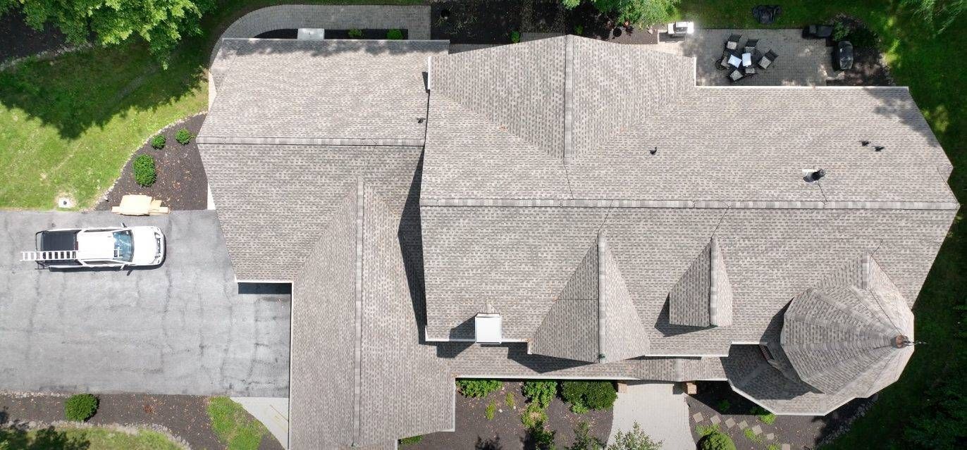 Overhead view of a house with a gray roof, driveway, and a white vehicle. Lush green lawn surrounds the home.