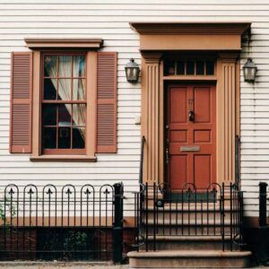 Brown door and window trim on a white house, with matching shutters and black wrought iron fence.
