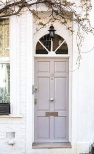 Gray front door with arched window and vine, set in white brick facade.