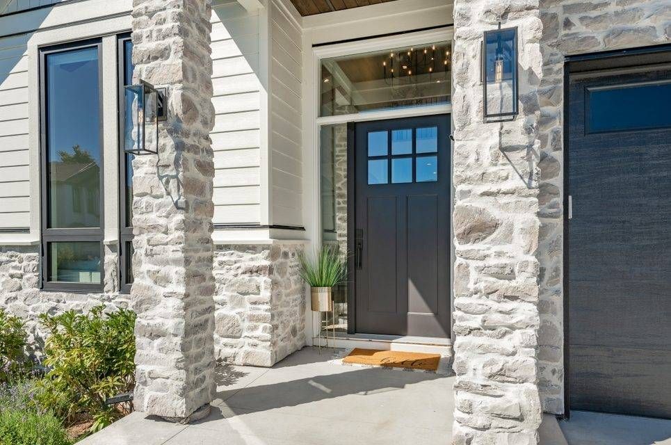 Gray stone entry with black door, sidelight, and garage door. Lantern lights flank the entry.