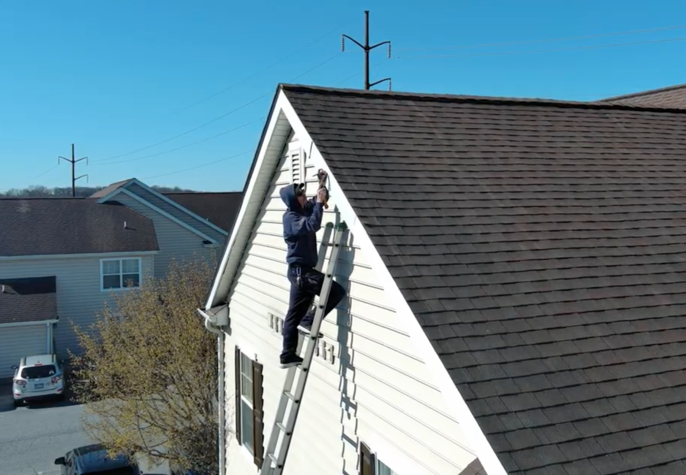 Person on a ladder, installing something on the side of a house. The sky is blue.