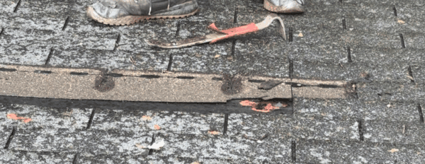 A person's feet, a crowbar, and damaged roofing shingles, presumably during a roof repair.