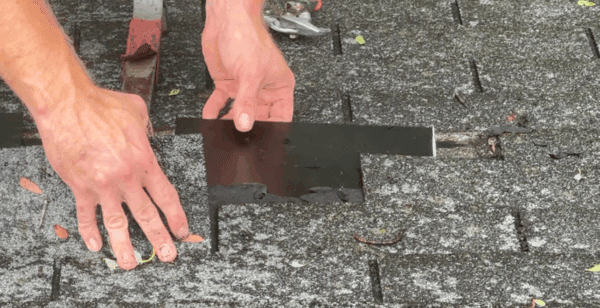 Hands installing a metal flashing on an asphalt shingle roof.